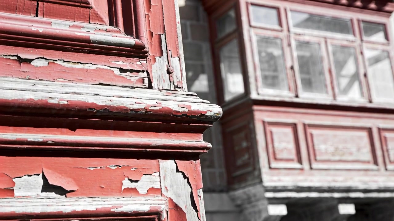 Telecamera in panoramica che rivela un pilastro di legno rosso sulla sinistra della facciata, mostrando vernice scrostata e finestre a bovindo.