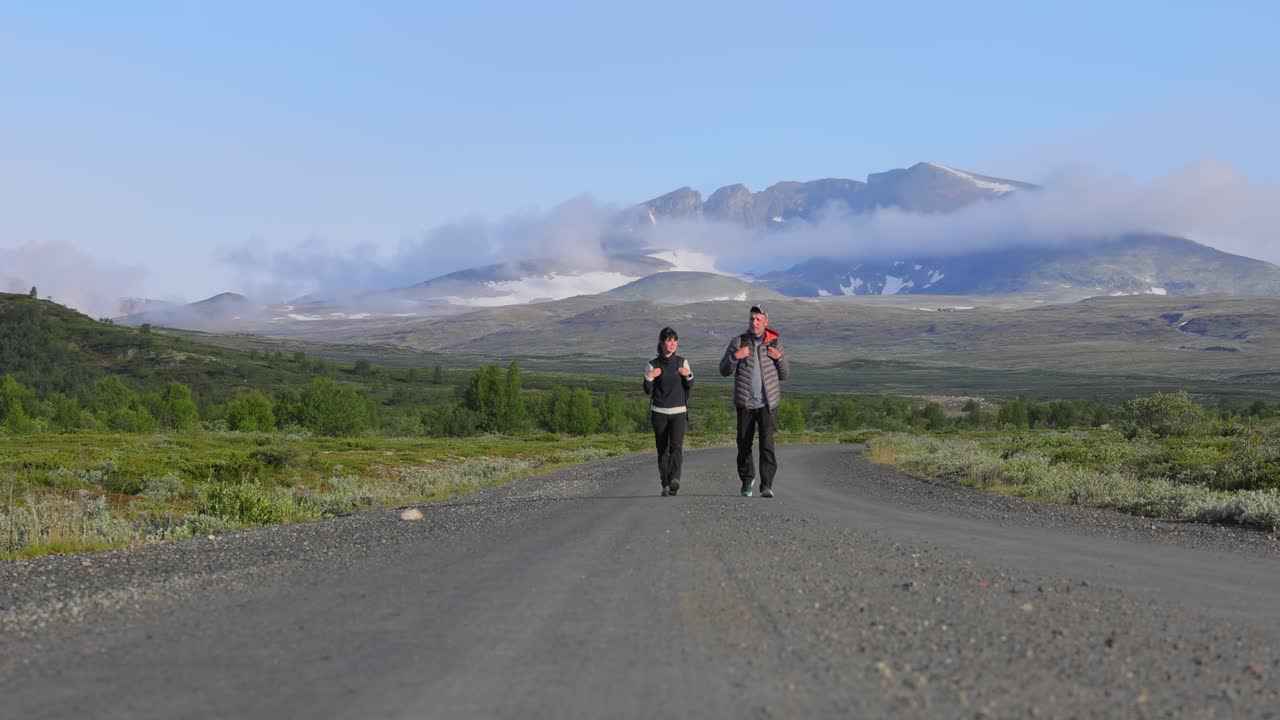 Sepasang Kekasih Mendaki dengan Ransel di Jalan dengan Latar Belakang Pegunungan. Taman Nasional Dovrefjell Sunndalsfjella adalah Taman Nasional di Norwegia. Pemandangan Alam Norwegia yang Indah.