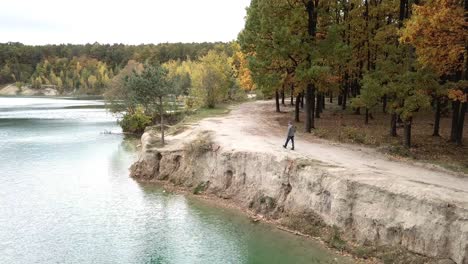 man walking along lake. aerial view of man walking along lake with forest