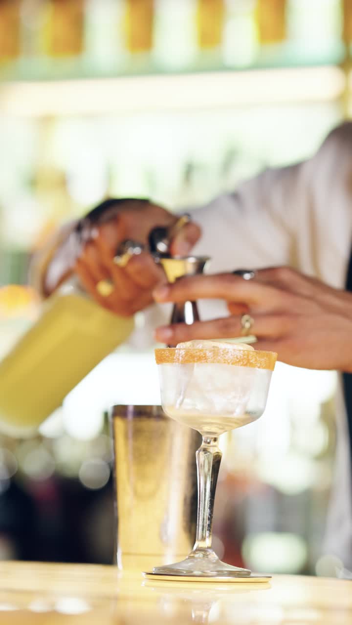 Bartender hælder væske fra jigger i cocktailglas på bar