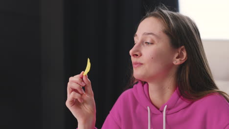 glückliche junge frau, die am schreibtisch sitzt und leckere kartoffelchips isst 2