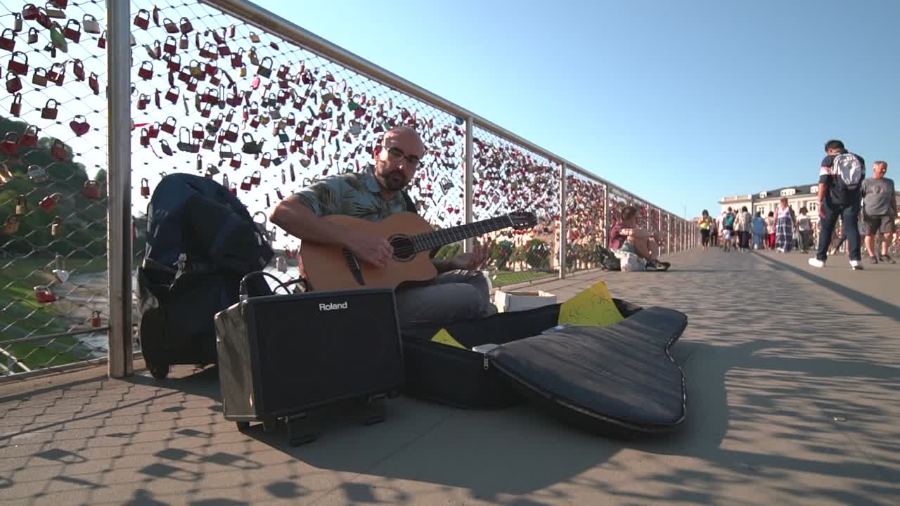 Adult Male Busker Playing Guitar On Makartsteg Bridge On Sunny Day In Salzburg. Low Angle