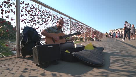 adult male busker playing guitar on makartsteg bridge on sunny day in salzburg. low angle