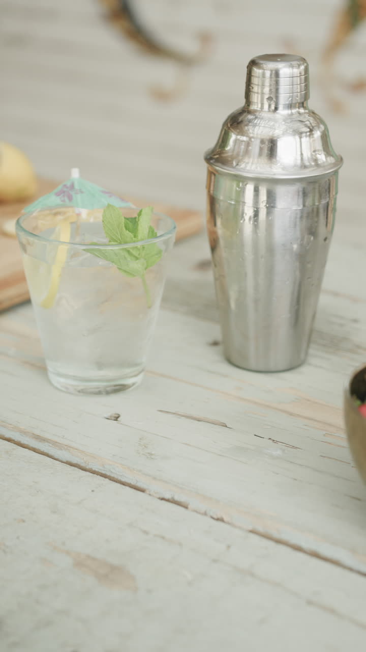Vertical video of cocktail, cocktail shaker and ingredients on bar at beach bar, slow motion
