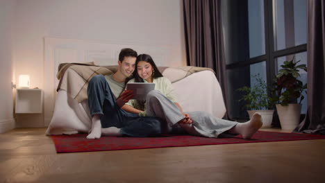 couple watching interesting movie on tablet while sitting on the floor at home 1