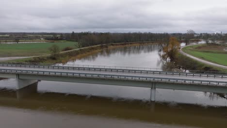 aerial establishing view of high water in springtime, barta river flood, brown and muddy water, overcast day, wide drone shot moving forward over the concrete bridge