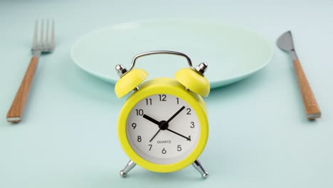 intermittent fasting, diet, lunch time concept. yellow alarm clock, empty plate and cutlery.