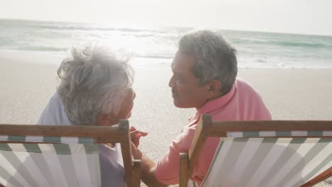 Feliz-Pareja-Hispana-Mayor-Besándose-Y-Relajándose-En-Las-Tumbonas-De-La-Playa-Al-Atardecer