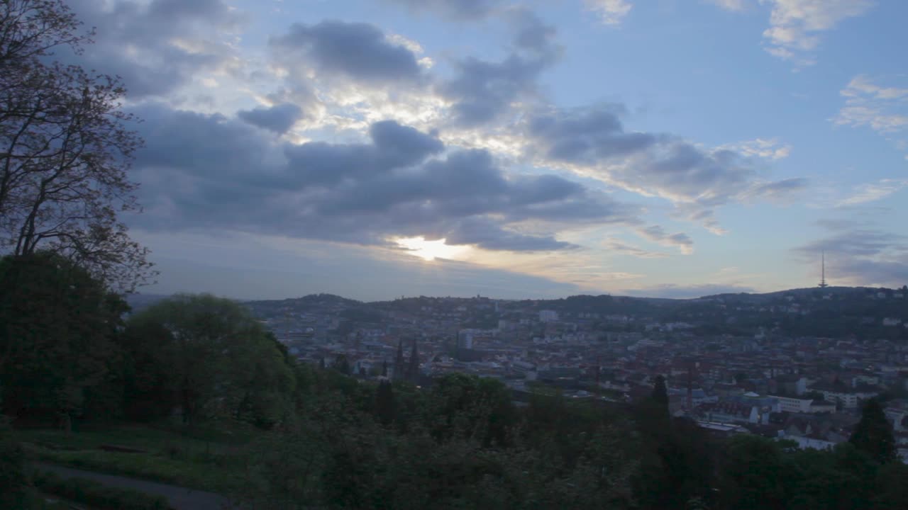 Sunset view of a cityscape with cloudy sky and surrounding hills, creating a serene atmosphere