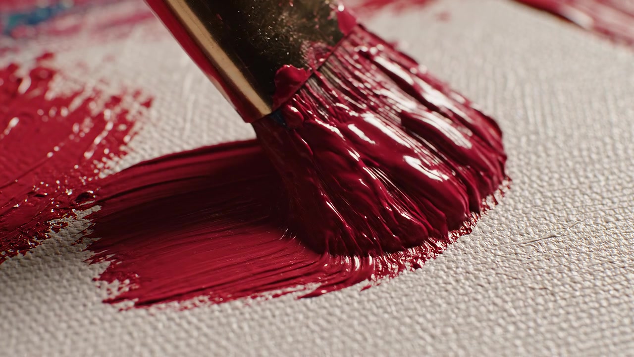 Primo piano di un pennello che applica pittura rossa densa su tela bianca