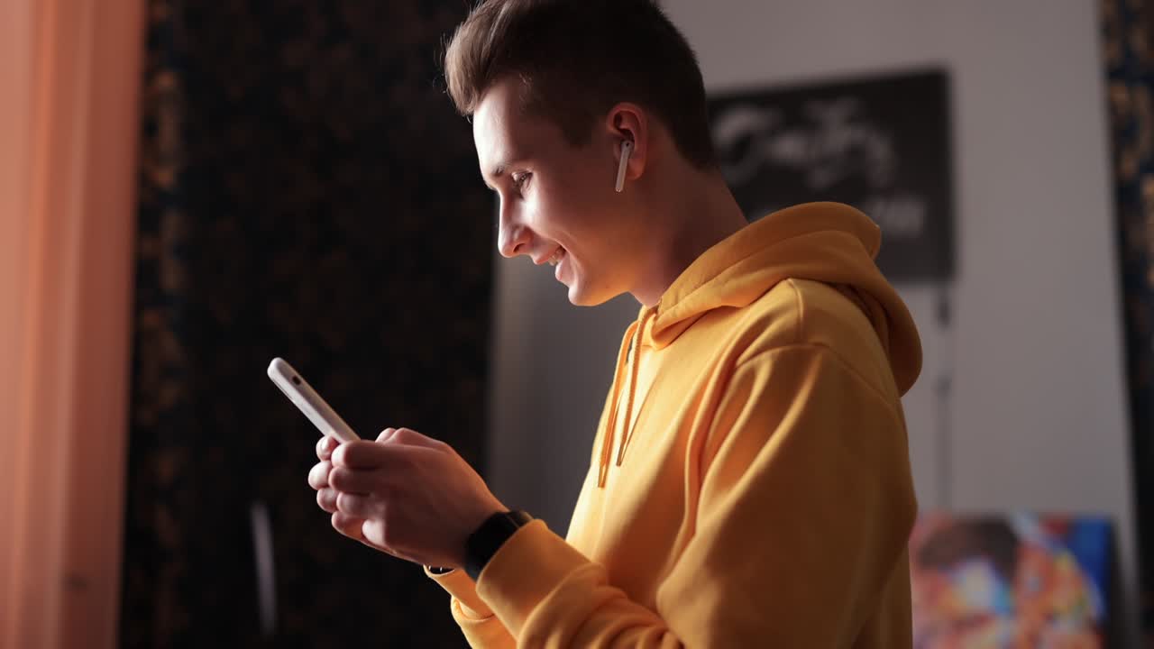 집에서 스마트폰과 이어폰을 사용하는 노란색 후디를 입은 남자