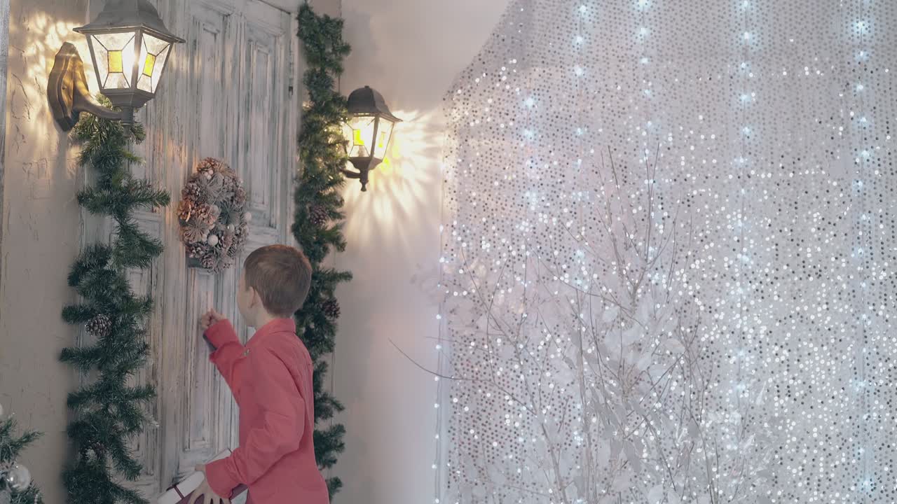 un niño rubio llama a una vieja puerta de madera con una caja de regalo