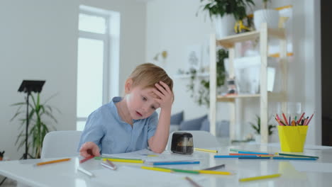 the boy sitting at the table in the living room writes a letter to his father and draws a picture of the family with a pencil