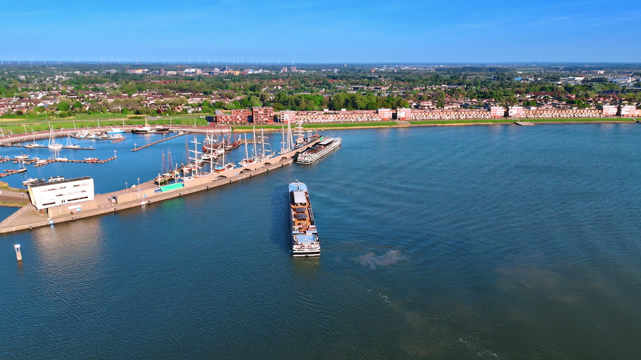 Flying closer to the port on Lake Markemeer. Ferry moves to the berth. Panorama of Lelystad, the Netherlands at backdrop.