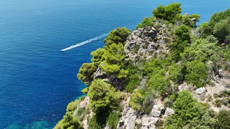 Aerial-shot-of-a-boat-near-the-rugged-cliffs-of-Corfu-Island,-Greece,-highlighting-the-clear-blue-Ionian-Sea