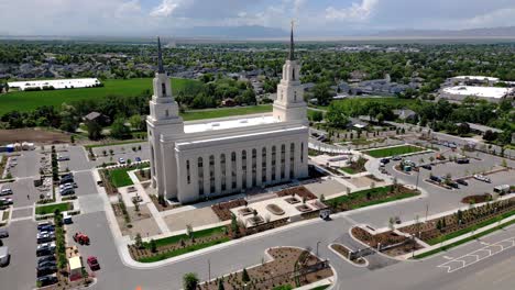 drone disparó viendo layton lleno lds templo mormón moviéndose alrededor a la izquierda injuriando vista completa de la ciudad en medio de un día soleado coches en el estacionamiento y conduciendo por la carretera