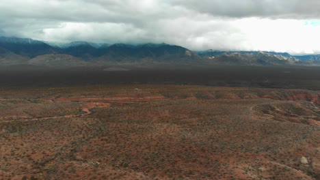 Toma-Aérea-De-Un-Paisaje-Seco-Y-Desolado-Con-Las-Montañas-Rocosas-Al-Fondo-En-Un-Día-Nublado