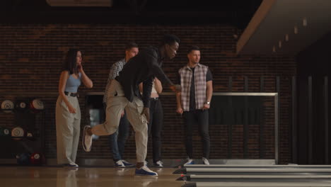 a young black man makes the final throw with a bowling ball and wins the game with the support and joy of his friends of different nationalities. rejoice and celebrate the victory