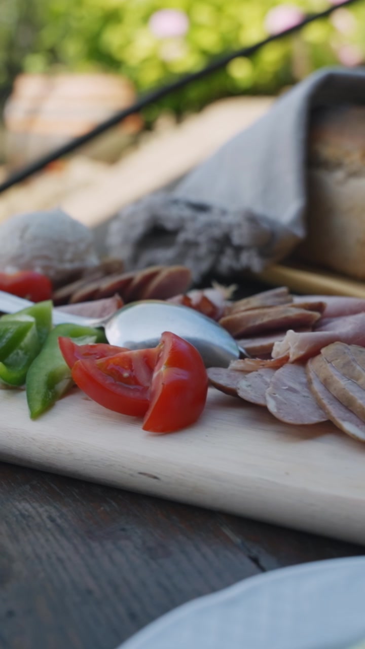 Rustikk charcuterie med skivet kjøtt, tomater, paprika, egg og håndverksbrød i naturlig dagslys. Perfekt vertikal nærbildevideo for mathistorier.