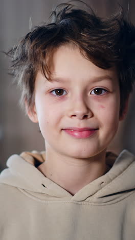 handsome smiling boy in beige hoodie smiling to camera. dark-haired teenager posing at the blurred backdrop of christmas tree indoors. vertical video