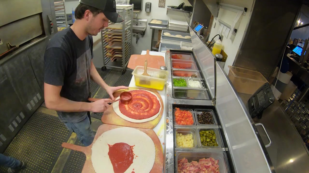 Time-lapse del personale di cucina che prepara pizze nella cucina di una pizzeria-ristorante a conduzione familiare.
