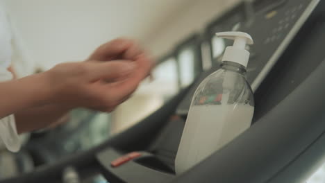 gros plan des mains à l'aide d'un désinfectant pour les mains et d'appareils d'exercice dans la salle de sport