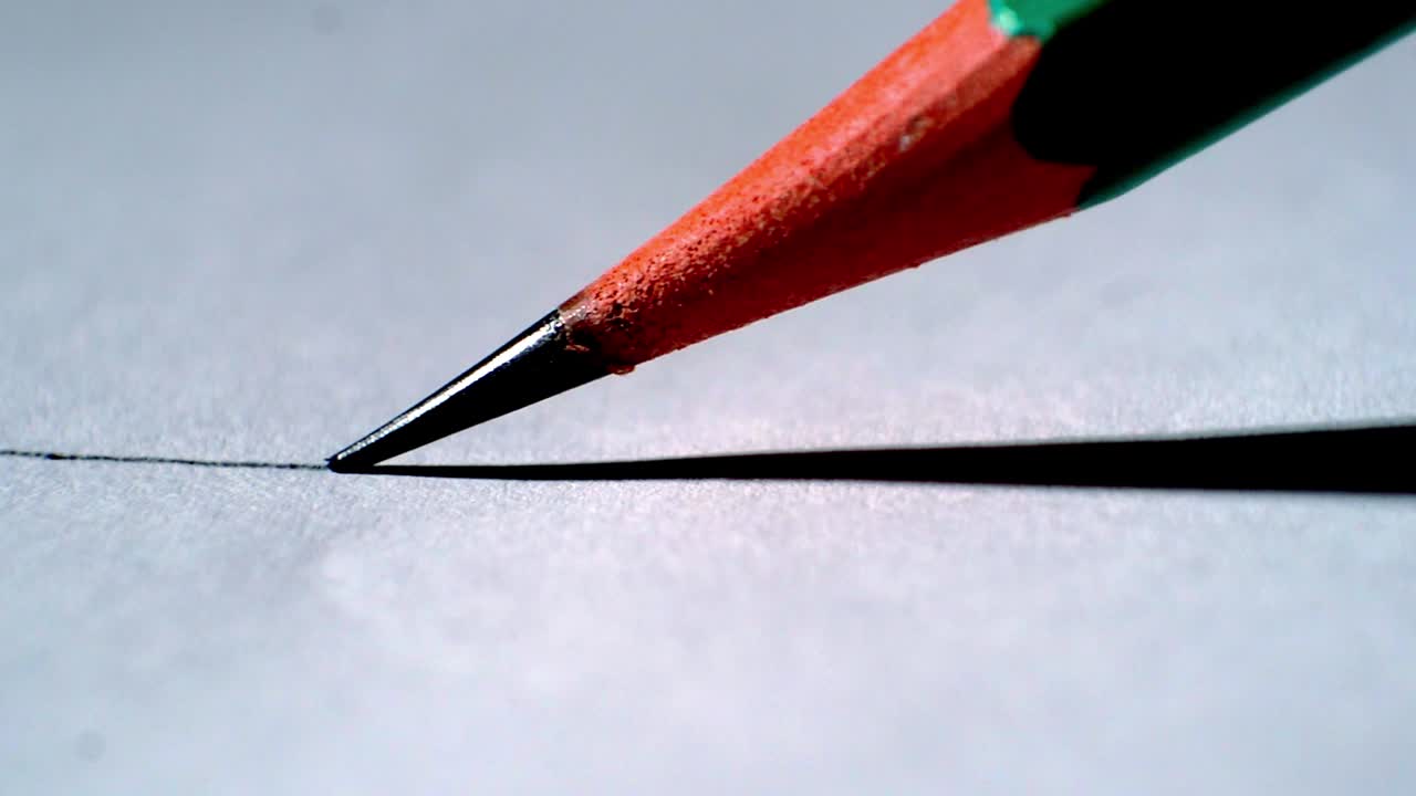 Macro close‑up of pencil drawing straight line on paper as tip suddenly breaks mid‑stroke