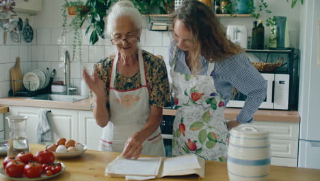 young woman and grandmother reading old recipe book in home kitchen