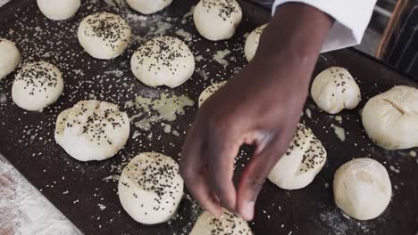 Diverse-bakers-working-in-bakery-kitchen,-sprinkling-poppy-seeds-on-rolls-in-slow-motion