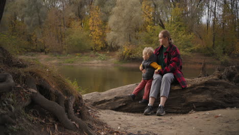 early fall in forest people are walking at good weather mother and child are sitting on shore of river family walk at nature