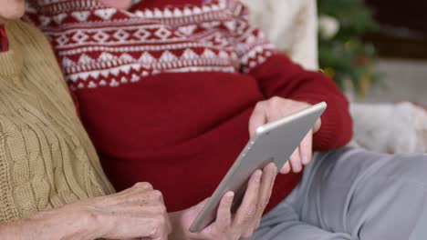 happy senior couple sitting on sofa and using digital tablet at christmas