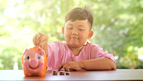niño asiático con una sonrisa feliz diversión poniendo monedas en una alcancía, cámara lenta. fondo bokeh. ahorro de dinero y recolección de dinero para el futuro.