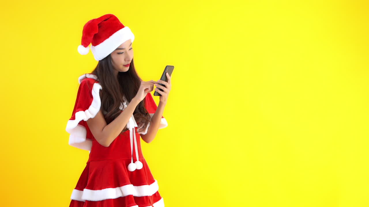 Smiling young woman Santa girl Christmas costume Using mobile phone typing SMS message isolated on yellow background
