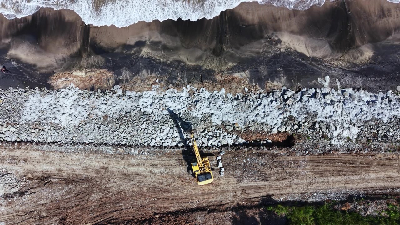 Construction work is taking place on a beach where rocks are being placed along the shore to prevent erosion during high tide