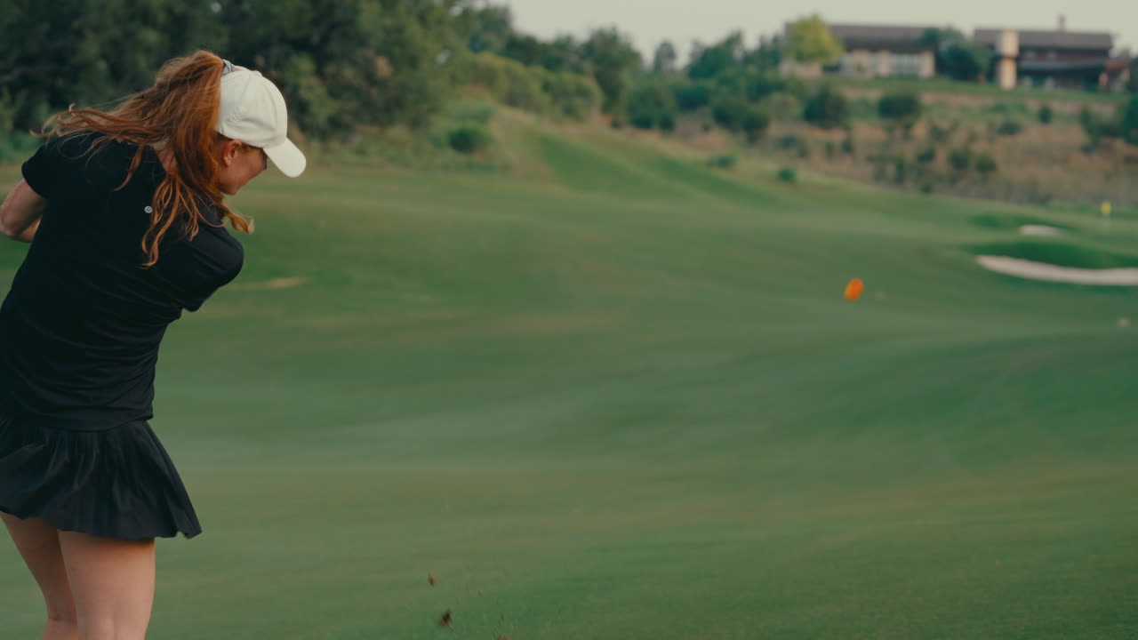 Tight slow motion shot of a female golfer hitting an approach shot with a hybrid club on the fairway. The clip highlights detailed swing mechanics, focus, and technique on a lush course.