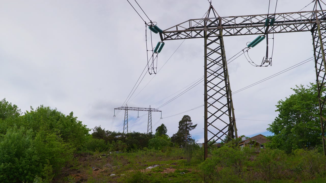 High-voltage power lines stretch across a green hillside in Norway, framed by dense trees. Suitable for energy and infrastructure topics.