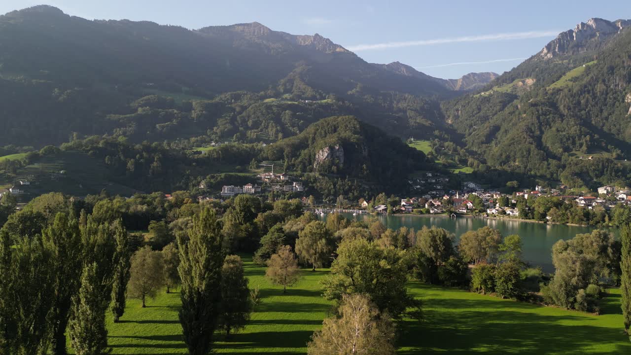 panorámica aérea de un hermoso bosque, lago y montañas que rodean un pequeño pueblo en suiza
