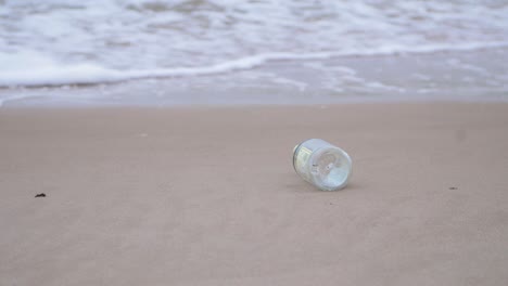 Empty-glass-bottle-on-the-beach,-trash-and-waste-litter-on-an-empty-Baltic-sea-white-sand-beach,-environmental-pollution-problem,-overcast-day,-medium-shot