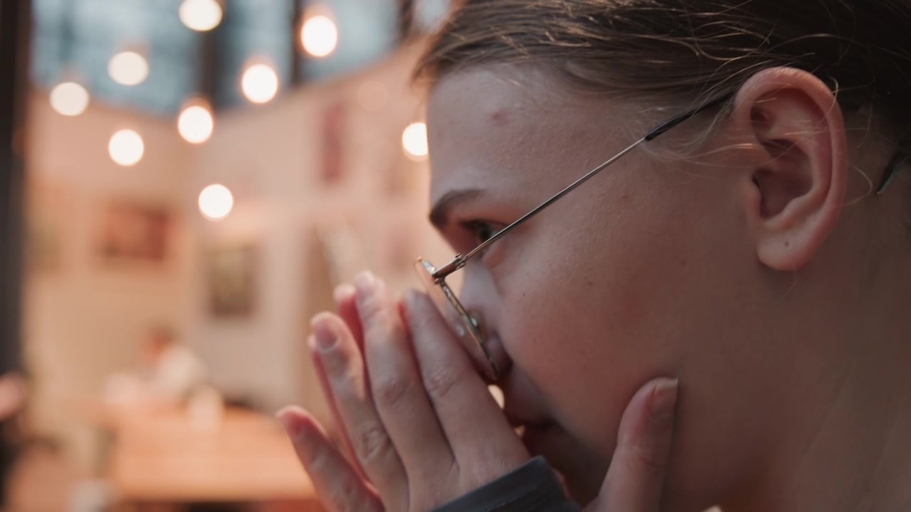 Close-up van een vrouw die warme koffie drinkt in een uitnodigend café. Portret van een dame die een latte proeft te midden van een gezellige cafésfeer. Elegante vrouw met een ronde bril geniet van een warme drank in een charmante cafésfeer.