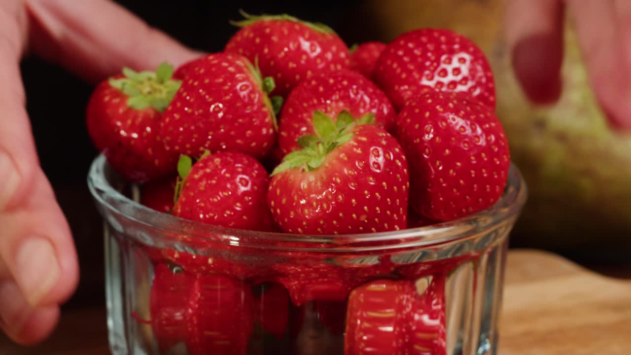 Hands Placing a Bowl of Fresh Red Strawberries on a Wooden Table