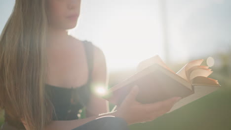 sunlight reflects on book held by woman seated outdoors with legs crossed, wind gently blows through pages as she flips to another page thoughtfully, background is softly blurred