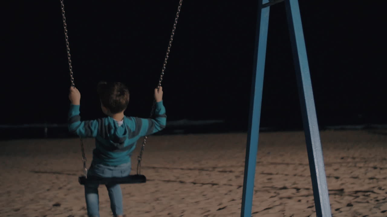niño balanceándose en la noche y mirando al mar oscuro