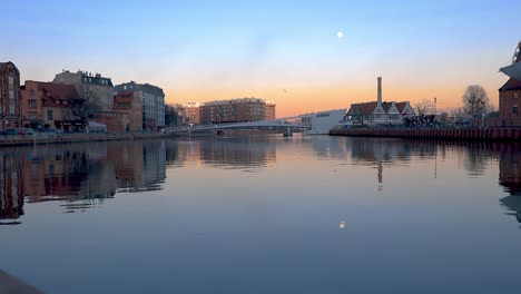 Goldene-Stunde-Panoramische-Aufnahme-Des-Stadtbildes-Am-Flussufer-Und-Der-Fußgängerbrücke-Im-Hintergrund-Von-Danzig-Polen