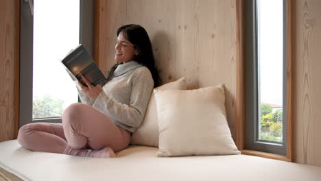 relaxing at home, woman reading book by window on cozy rainy day, copy space