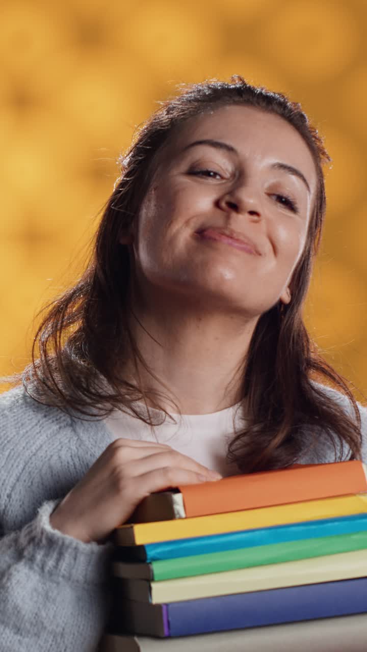 Jovem segurando pilha de livros coloridos e fazendo sinal de positivo