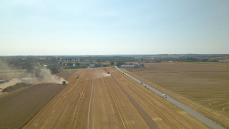 Landmaschinen,-Die-Reife-Ernten-Auf-Dem-Feld-In-Kielno,-Polen,-Mit-Fahrzeugen-Auf-Der-Straße-Ernten---Absteigende-Drohnenaufnahme