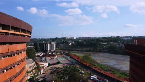 Flying-in-middle-of-buildings,-overlooking-traffic-on-the-coast-of-Lac-Central,-in-sunny-Yaounde,-Cameroon