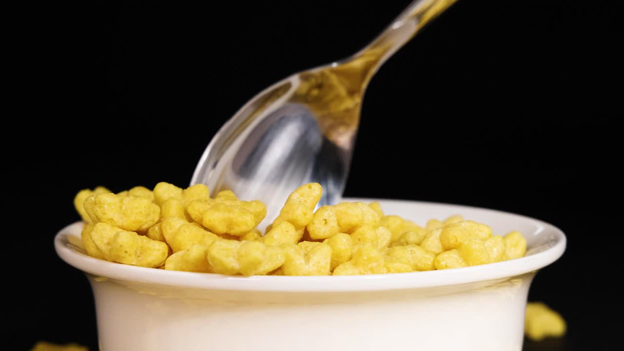 A spoon lifts crunchy, star-shaped cereal from a bowl against a black background, highlighting texture and motion