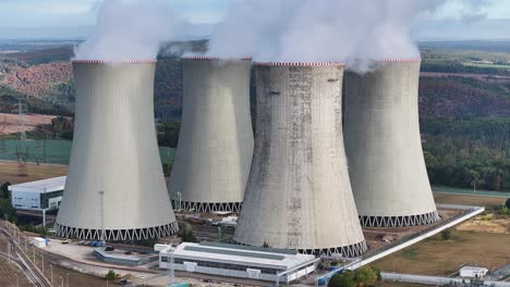 aerial view of multiple huge nuclear power plant cooling towers emit dense vapor