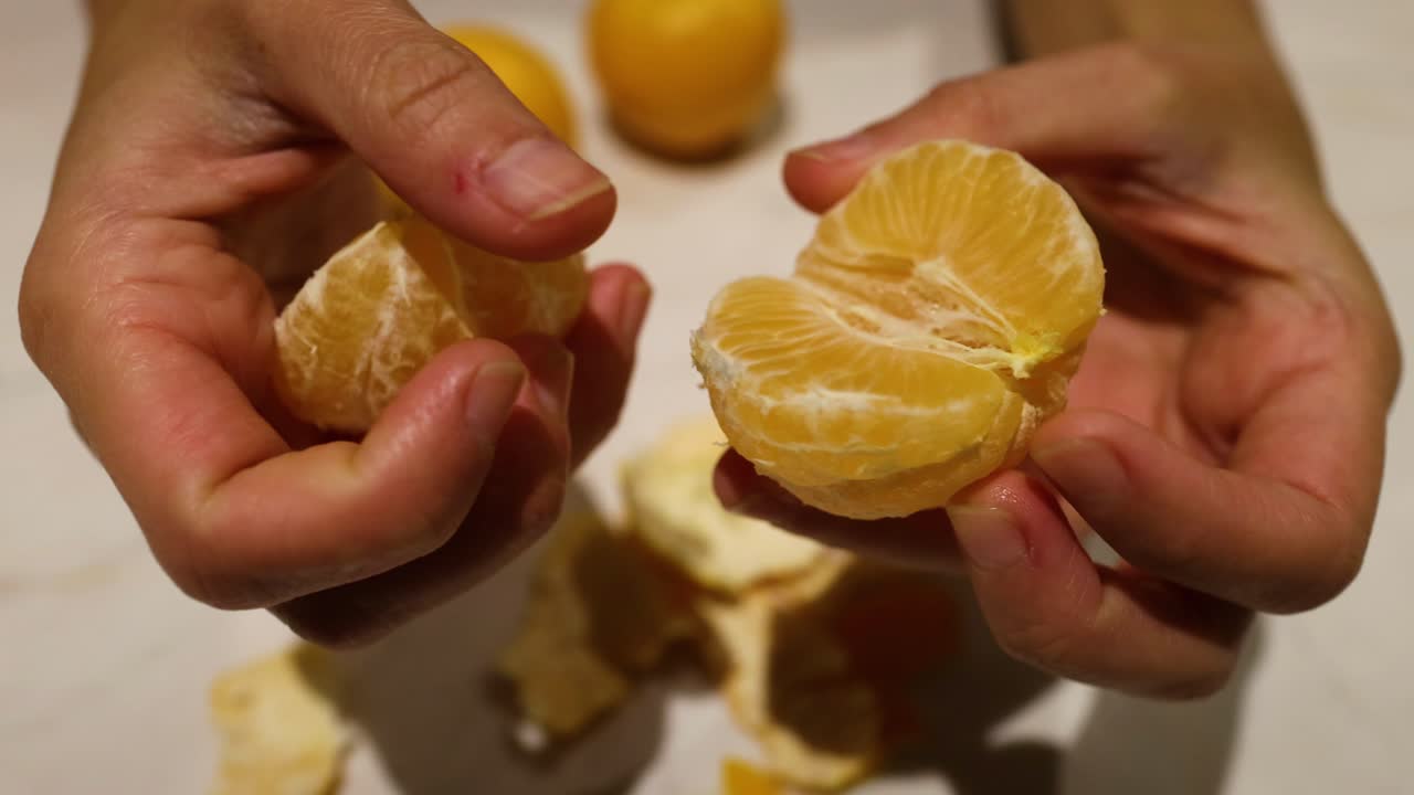 las manos pelando y separando una naranja